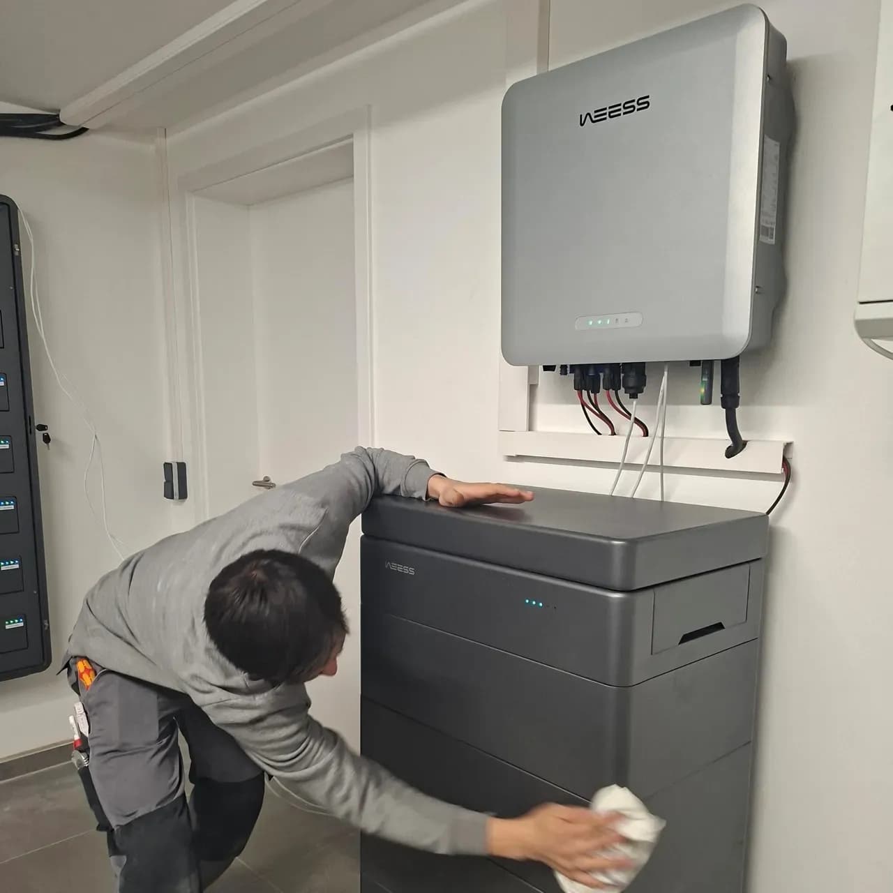 Techniker reinigt WEESS Batteriespeicher unter installiertem Wechselrichter