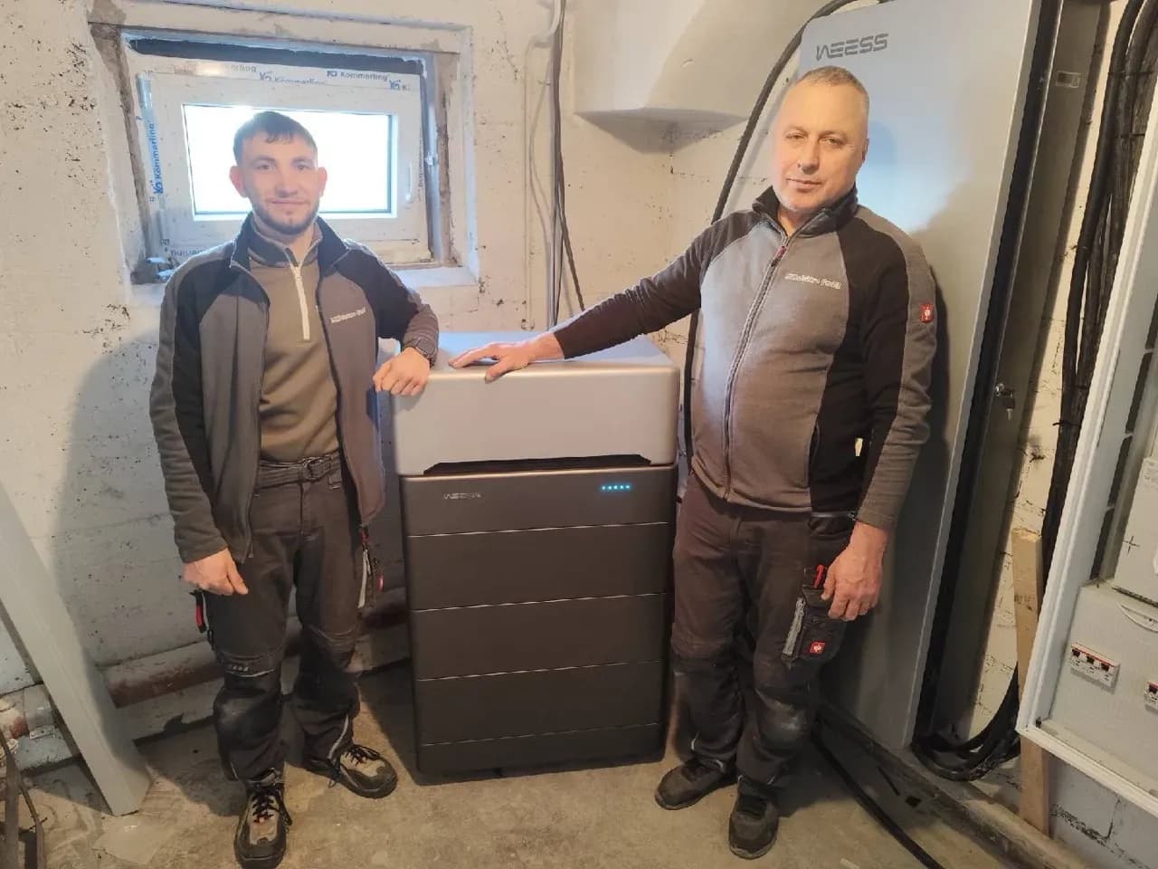 Installateure neben installiertem WEESS Batteriespeicher im Technikraum eines Wohngebäudes