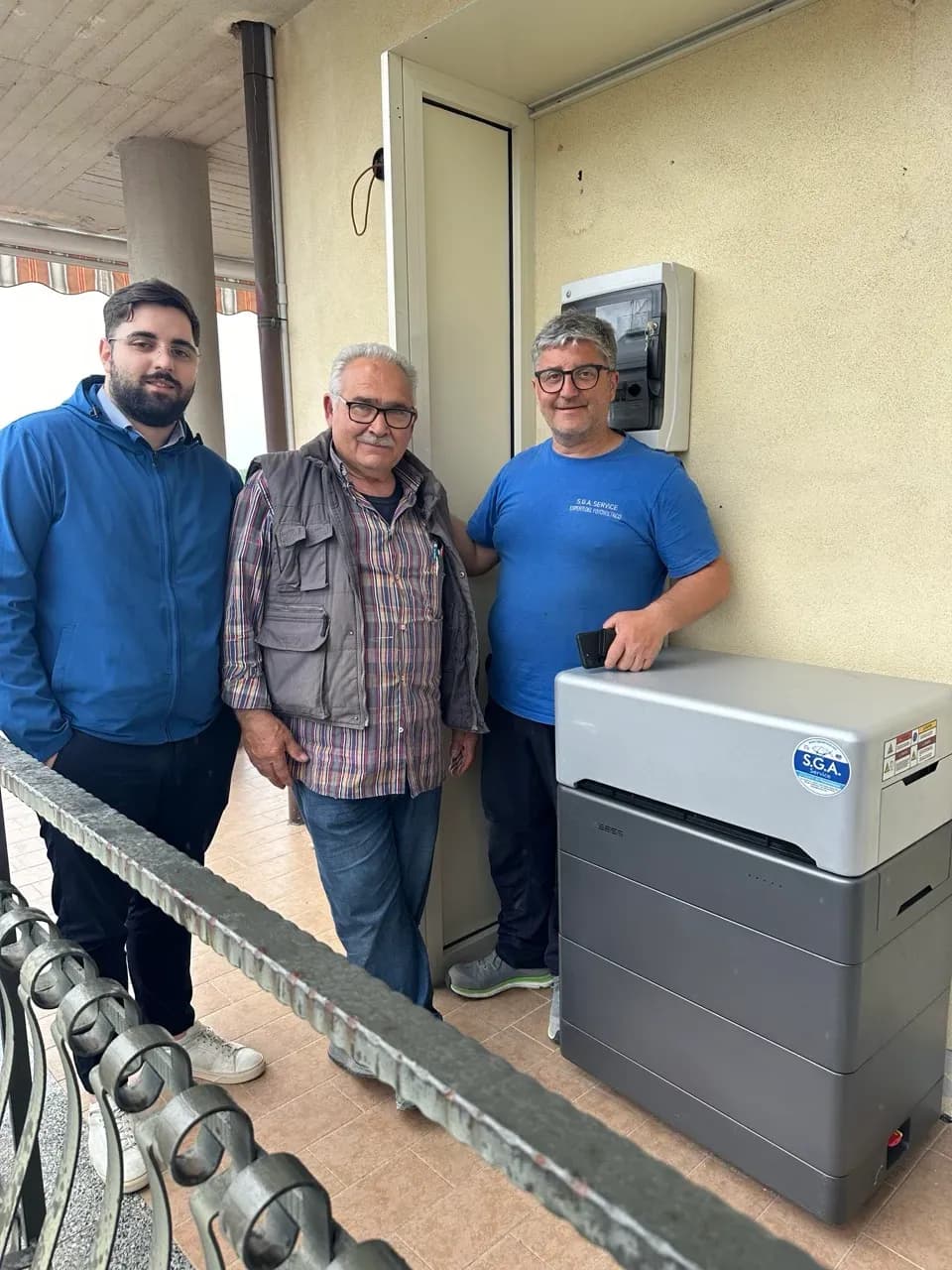 Kunde und Installateure neben installiertem WEESS Batteriespeicher auf Balkon eines Wohngebäudes